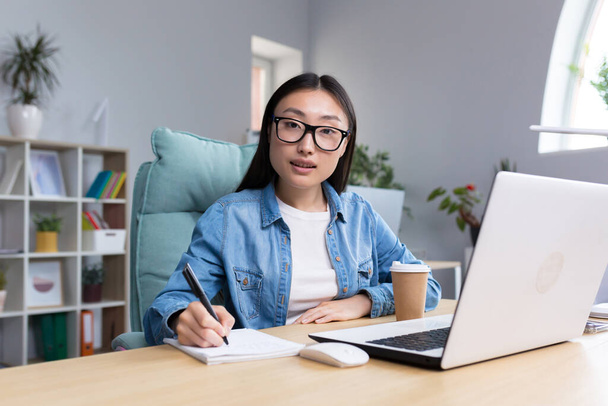 Portrait of young asian woman in office doing paperwork, smiling and looking at camera business woman with laptop in asia. - Φωτογραφία, εικόνα