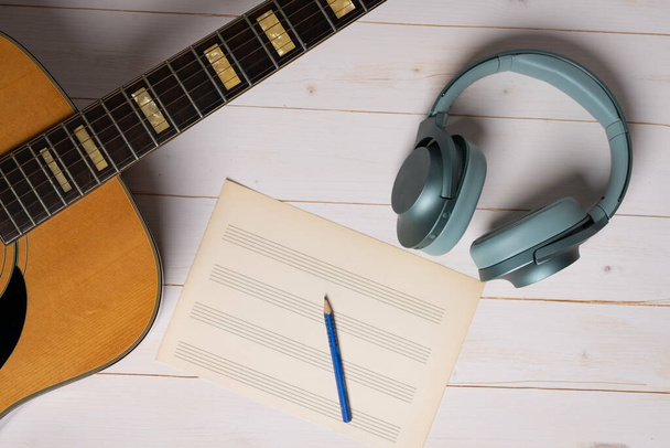 Music recording scene with guitar, empty music sheet, pencil and headphones on white wooden table - Photo, image