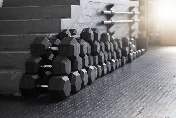 Closeup of a group of gym weights on the floor in an empty health and sports club. Macro view of dumbbells barbell weights in a dark exercise room. Get to the gym to increase your health and fitness. - Foto, afbeelding