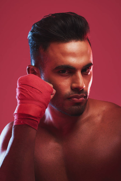 Portrait of one fit and strong handsome mixed race kickboxer isolated against a red studio background and getting ready to fight. Hispanic man posing shirtless in a punching stance. Focused on target. - 写真・画像