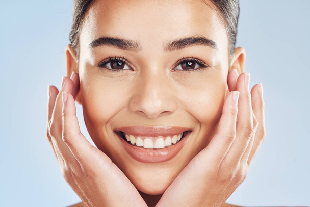 Closeup face beautiful young mixed race woman. Attractive female touching her face in studio isolated against a blue background. A skincare regime to keep your skin soft, smooth, glowing and healthy. - Фото, изображение