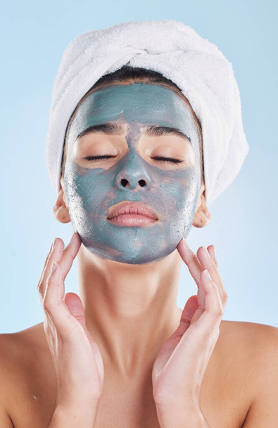 Schöne junge Mischlingshündin, die sich isoliert im Studio vor blauem Hintergrund eine Gesichtsmaske aufsetzt. Attraktive Frau mit einem Handtuch auf dem Kopf nach dem Duschen. Ihre Hautpflege hält sie frisch. - Foto, Bild