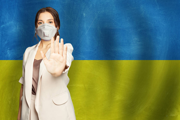 Retrato de jovem mulher grave em máscara protetora contra fundo bandeira ucraniana - Foto, Imagem