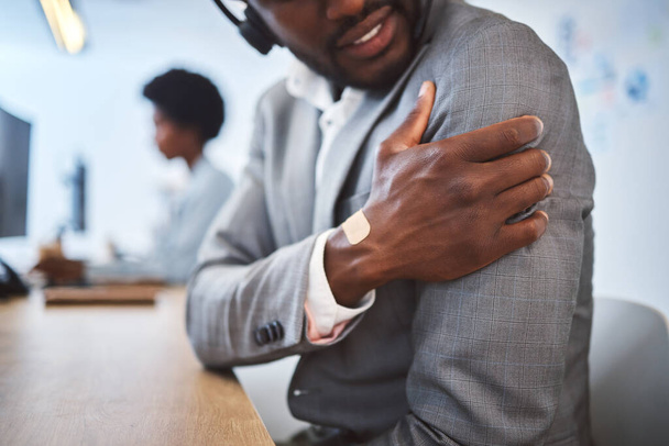 Closeup of one stressed african american businessman suffering with arm and shoulder pain in an office. Entrepreneur rubbing muscles and body while feeling tense strain, discomfort and hurt from bad - Foto, imagen