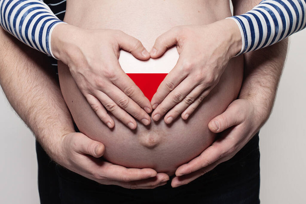 Polish family concept. Man embracing pregnant woman belly and heart with flag of Poland colors closeup - Foto, Imagem