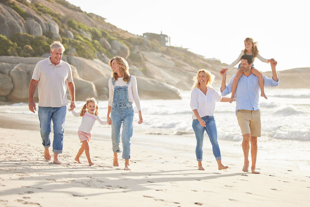 Monen sukupolven perhe pitää toisiaan kädestä ja kävelee rannalla yhdessä. Valkoihoinen perhe, jossa kaksi lasta, kaksi vanhempaa ja isovanhemmat nauttivat kesälomasta. - Valokuva, kuva