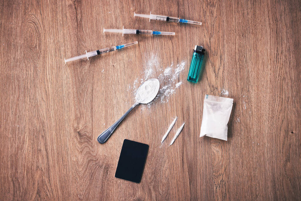 Een lepel met heroïne, spuiten met met, een blauwe aansteker, een tas en een bankkaart op een houten tafel. Een zeer verslavend pijnstiller gemaakt van morfine, illegaal gebruikt als verdovend middel dat euforie veroorzaakt.. - Foto, afbeelding