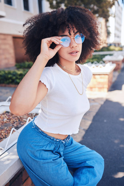 Young stylish mixed race woman with curly natural afro hair wearing trendy glasses outside. One female only looking carefree, cool and confident. Happy fashionable hispanic woman relaxing in the city. - Fotografie, Obrázek