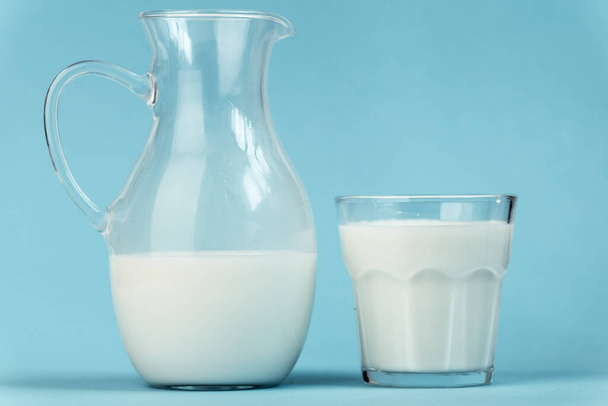 Jug and glass full of milk on blue background. Benefits of dairy products concept - Zdjęcie, obraz