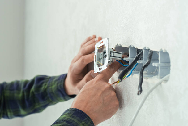 Electrician mounts a new socket on a white wall. Renovation process in a new apartment - Foto, Bild