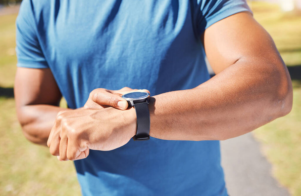 Closeup of unknown fit active mixed race man using a smartwatch to time a workout and check his heart rate after training outdoors alone. Muscular hispanic athlete monitoring calories during exercise. - Foto, immagini