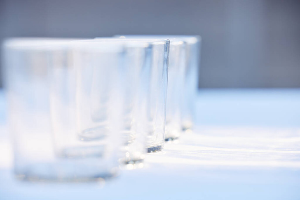 Closeup of a row of clear empty drinking glasses reflecting sunlight. Set of transparent glasses for drinks, whisky or other beverages on a table. - Foto, Imagem