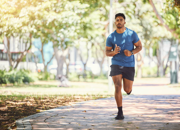 One active young indian man exercising outdoors. Handsome male athlete enjoying a jog or run for cardio training workout. Determined to build muscle and endurance for fitness and wellness goals. - Photo, Image