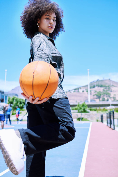 Πορτρέτο μιας μοντέρνας γυναίκας μικτής φυλής με ένα αφρο να κρατάει ένα μπάσκετ και να ποζάρει σε ένα γήπεδο έξω. Μοντέρνος Ισπανός με σγουρά μαλλιά που νιώθει αυτοπεποίθηση. Αφροαμερικανός δείχνει δρόμο στυλ. - Φωτογραφία, εικόνα