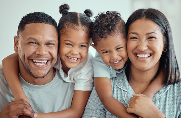 Portrait d'une heureuse jeune famille métissée avec deux enfants en pyjama et assis à la maison ensemble. Petite fille mignonne et garçon embrassant leur mère et leur père par derrière. - Photo, image