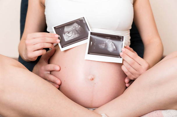 Porträt eines jungen glücklichen Ehepaares mit Ultraschallbild. Diverse Männer und schwangere Frauen zeigen Sonogramme am Kind, aufgeregt für die Elternschaft. Erziehungskonzept. - Foto, Bild