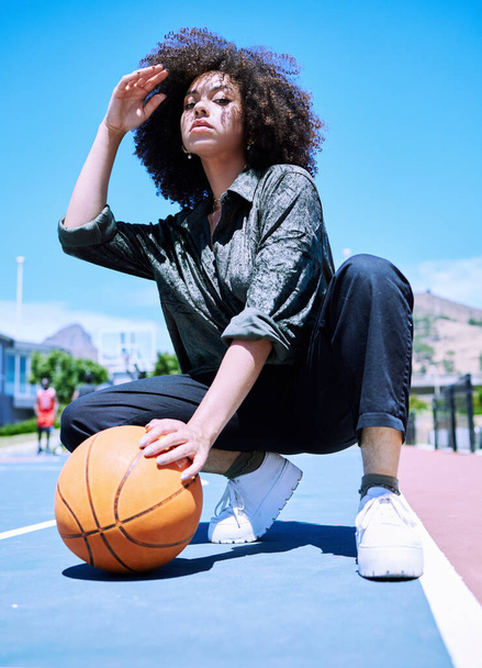 Χαμηλή άποψη ενός νεαρού με αυτοπεποίθηση μικτή φυλή γυναίκα μπασκετμπολίστας στέκεται στο γήπεδο ετοιμάζεται να παίξει. Ισπανίδα μπασκετμπολίστας μια μέρα στο γήπεδο με το σγουρό της αφρό - Φωτογραφία, εικόνα