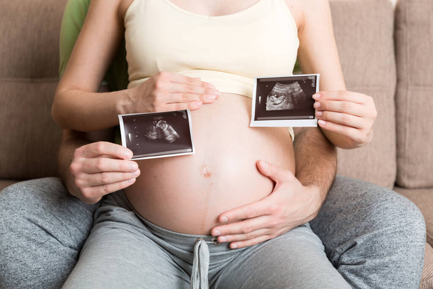 Porträt eines jungen glücklichen Ehepaares mit Ultraschallbild. Diverse Männer und schwangere Frauen zeigen Sonogramme am Kind, aufgeregt für die Elternschaft. Erziehungskonzept. - Foto, Bild