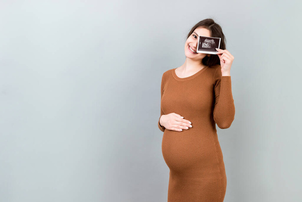 Nette schwangere Dame posiert mit Baby Sonographie Foto in der Nähe farbigen Hintergrund. Konzept der Schwangerschaft, Gynäkologie, medizinische Tests, Müttergesundheit. - Foto, Bild