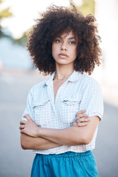 A young female mixed race woman standing with her arms crossed outside looking cool and confident with great style. Hispanic hipster woman with a curly afro in a cool outfit against a urban background - Foto, Imagen