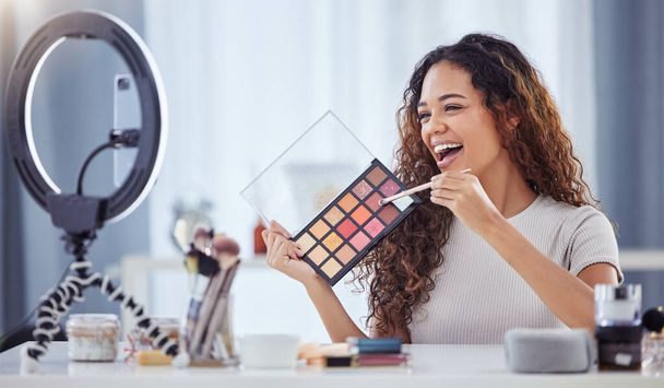 Eine hispanische Frau nimmt mit ihrem Handy eine Make-up-Anleitung für ihren Beauty-Blog auf, während sie zu Hause sitzt. Afroamerikanische Influencerin im Livestream: Kosmetiktest und Empfehlungen online - Foto, Bild
