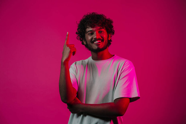 Young middle eastern man smiling and pointing finger upward isolated over pink wall - Fotó, kép
