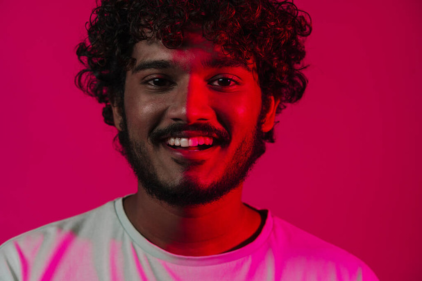 Fiatal közel-keleti férfi mosolyog, és nézi kamera fülhallgató elszigetelt rózsaszín fal - Fotó, kép