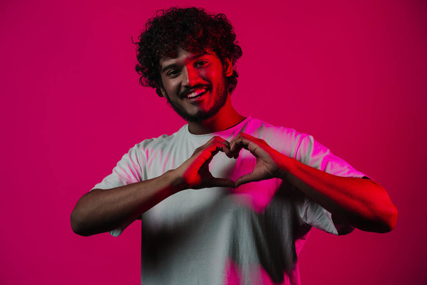 Young middle eastern man smiling and making heart gesture isolated over pink wall - Foto, Bild