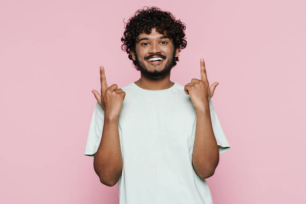 Young middle eastern man smiling and pointing fingers upward isolated over pink wall - Foto, immagini