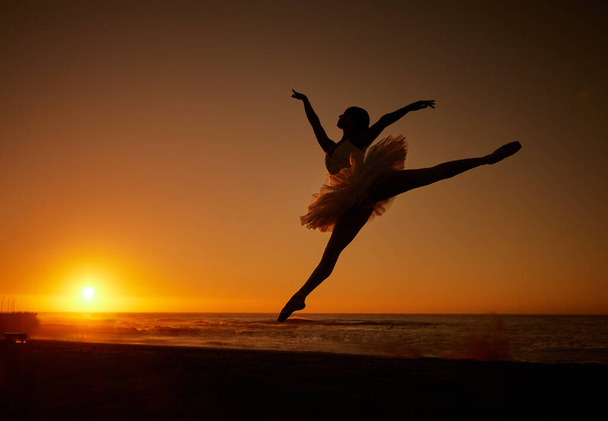 Силует балетної танцівниці в турі танцює на пляжі під час заходу сонця. Витончена балерина танцює і стрибає на відкритому повітрі
. - Фото, зображення
