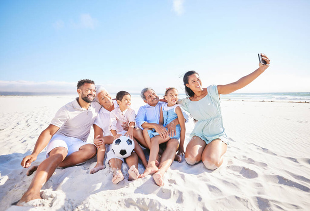 Família multi étnica tirando uma selfie para capturar e documentar belos momentos juntos. Família com dois filhos, dois pais e avós em videochamada enquanto jogava futebol na praia. - Foto, Imagem