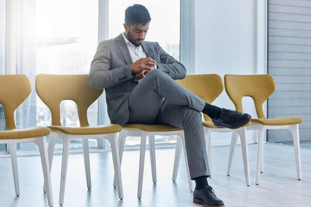 Egy fiatal indiai üzletember öltönyt visel, ellenőrzi az óráját, miközben egy széken ül és várja az interjút. A fickó türelmetlenül várja a megüresedett találkozót. A pontosság fontos. - Fotó, kép