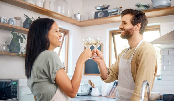 Young interracial couple sharing toast with wine glasses while wearing aprons and cooking together in kitchen at home. Young couple enjoying romantic homemade dinner for date night at home. - Foto, imagen