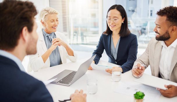Confident young asian businesswoman explaining plans and ideas to her diverse colleagues while going through paperwork during a meeting in an office boardroom. Happy businesspeople having a discussion - Photo, Image