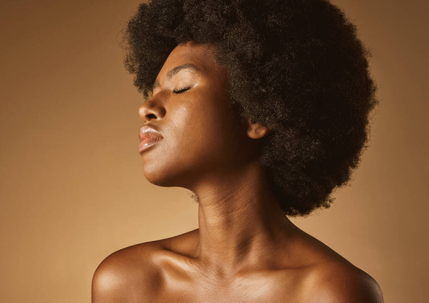 Confident African American woman with a natural afro posing against brown studio copyspace background. Young beautiful black female model looking trendy, powerful and sensual with smooth glowing skin. - Φωτογραφία, εικόνα