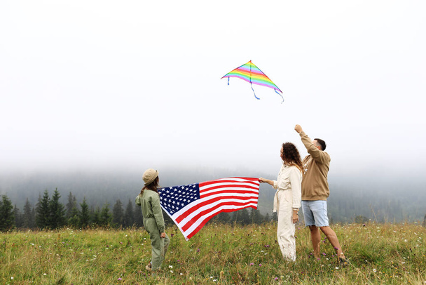 Patriotic holiday in United States of America. Happy family, parents and daughter child girl with American flag in nature on foggy mountains. The USA celebrate 4th of July - Photo, Image