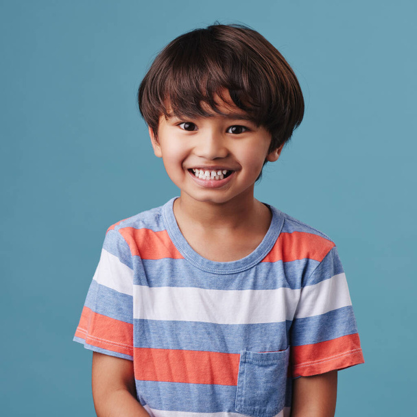 Portrét roztomilého malého asijského chlapce v neformálním oblečení, zatímco se usmívá a vypadá vzrušeně. Dítě stojí na pozadí modrého studia. Roztomilý šťastný chlapeček v bezpečí a sám. - Fotografie, Obrázek