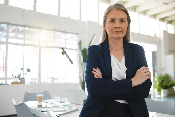Femme d'affaires caucasienne concentrée mature debout avec les bras croisés dans un bureau seul. Une femme gestionnaire confiante debout au travail. - Photo, image