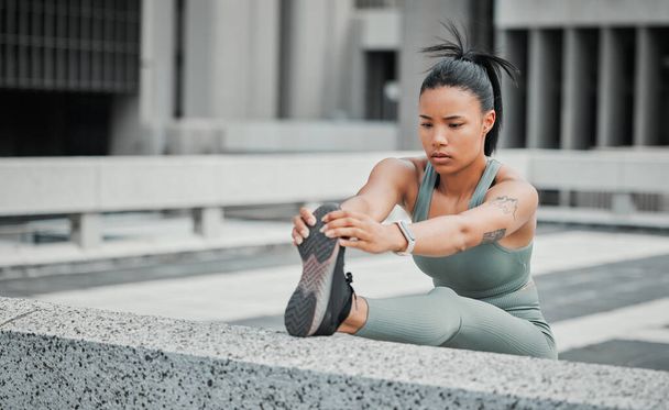 Young mixed race hispanic female athlete stretching her leg before a run outside in the city. Exercise is good for your health and wellbeing. Stretching is important to prevent injury. - Foto, Bild
