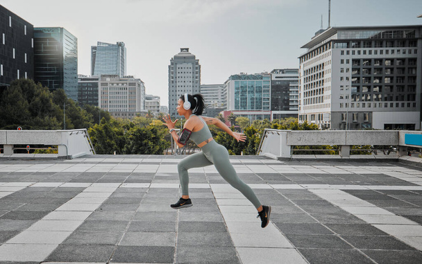 Young mixed race hispanic female wearing headphones listening to music and running outside in the city. Exercise is good for your health and wellbeing. - Foto, Imagem