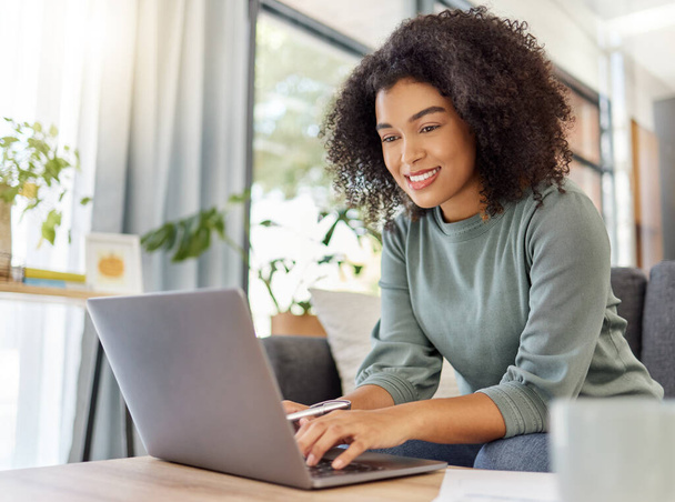 Young mixed race woman working on filling out forms while typing on a laptop at home. One hispanic female smiling while planning and sending an email alone in the lounge at home. - Foto, Bild