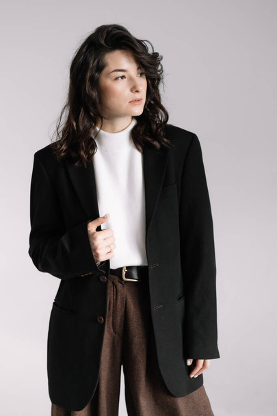 Attractive woman wear business look. Brunette model wear white shirt, black men's jacket and brown baggy pants. Winter, fall autumn or spring minimal outfit. - Foto, afbeelding