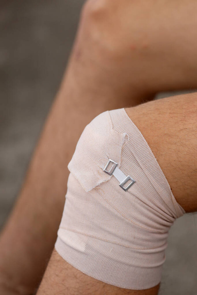 Knie des Jungen nach der Verstauchung mit einem Gummiband zum Schutz des beschädigten Gelenks - Foto, Bild