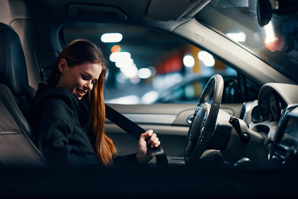 horizontale foto van een aardige vrouw zittend in een auto op de parkeerplaats met een veiligheidsgordel om. Hoge kwaliteit foto - Foto, afbeelding