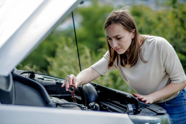 The woman pulls out a probe in her car engine to check the oil level. The woman manages the car herself. - Photo, image