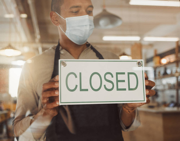 Business owner closing his store in covid lockdown. Businessman hanging a closing sign in his shop door. Boss advertising that his shop is closed in the pandemic. Shop owner wearing a mask. - Foto, Imagen