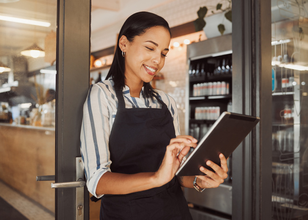 Businesswoman using a digital tablet in her restaurant. Cafe owner using an online app in her shop entrance. Confident business owner using a wireless device in her grocery store - Foto, Bild