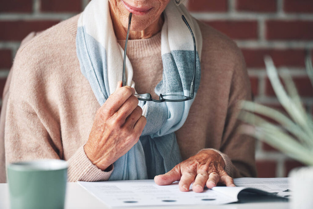 Dojrzała kobieta czytająca dokumenty ubezpieczeniowe w domu.Starsza kobieta czytająca dokumenty finansowe planująca emeryturę. Dojrzała kobieta trzyma okulary i czyta dokumenty.. - Zdjęcie, obraz