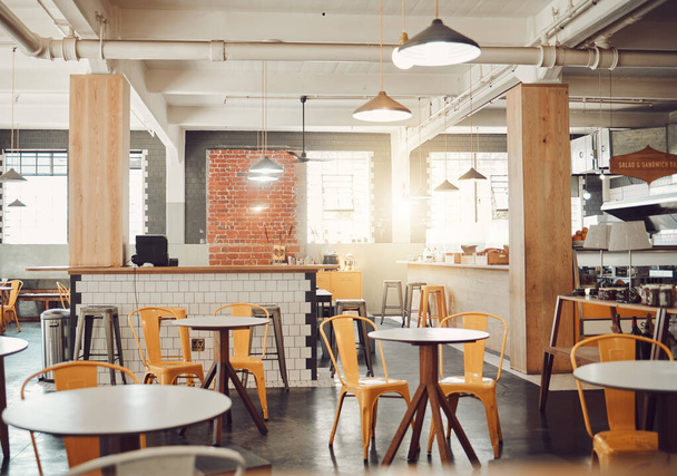 Interiér prázdné moderní kavárny nebo restaurace během dne. Kulaté stoly a žluté židle v rustikální kavárně. Otevřený prostor kavárna s vystavenými trubkami a závěsné závěsné světla. - Fotografie, Obrázek