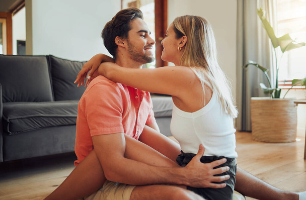 Happy caucasian couple being affectionate and enjoying romantic intimate moment while sitting on living room floor. Young woman sitting on top of boyfriend and putting her arms around him. - Foto, immagini